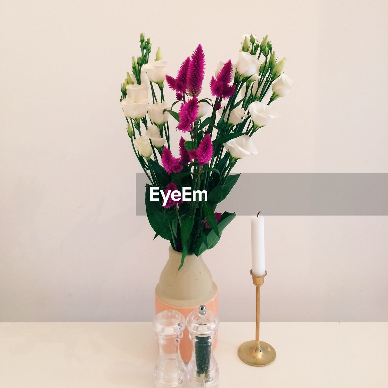 Flower vase and candle on table against white wall