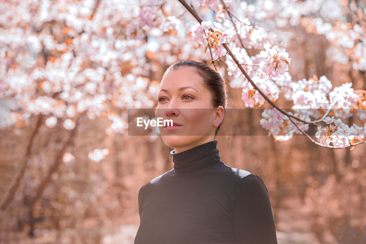 Portrait of young woman standing by cherry blossom tree
