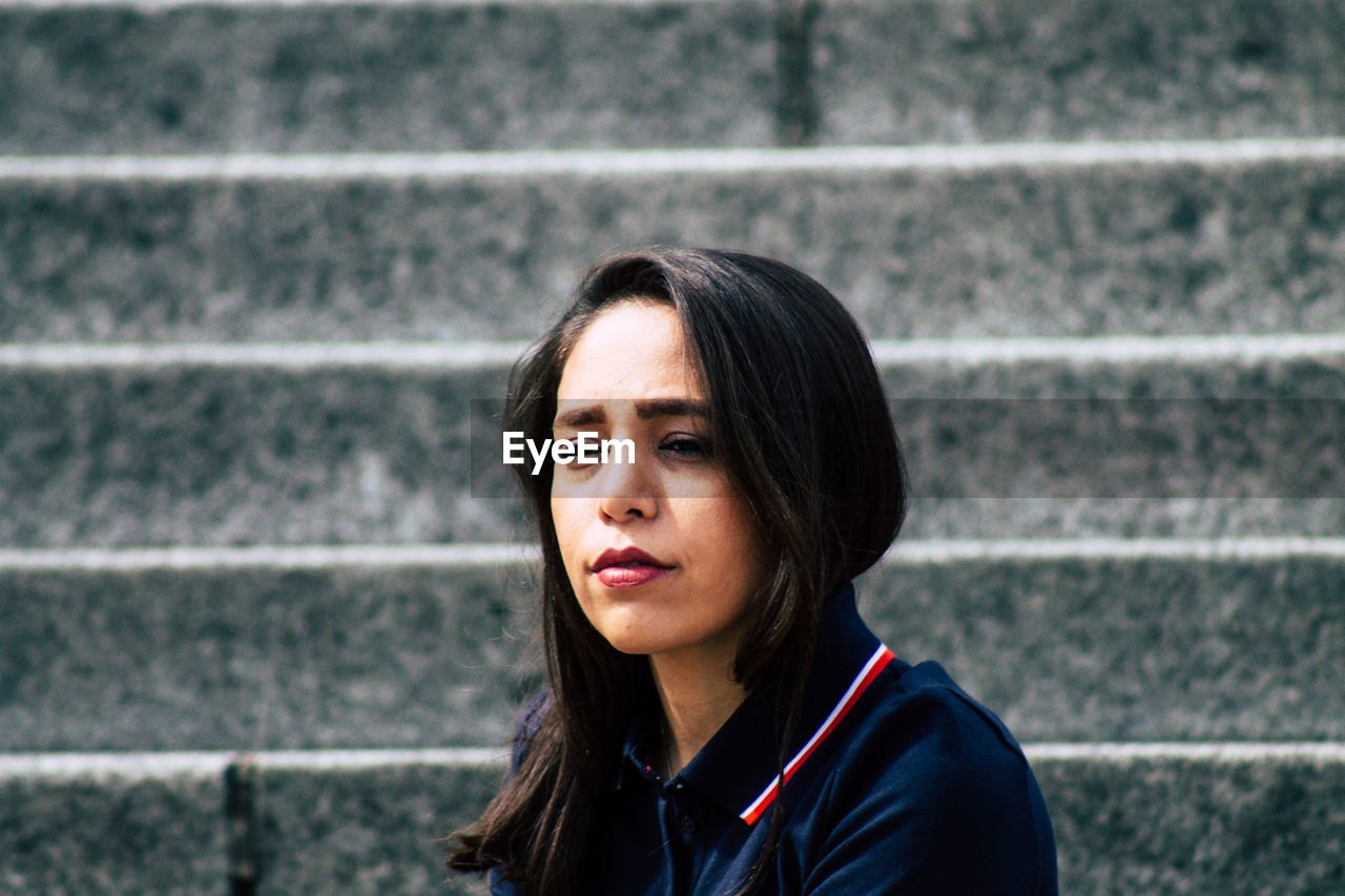 PORTRAIT OF YOUNG WOMAN STANDING AGAINST WALL