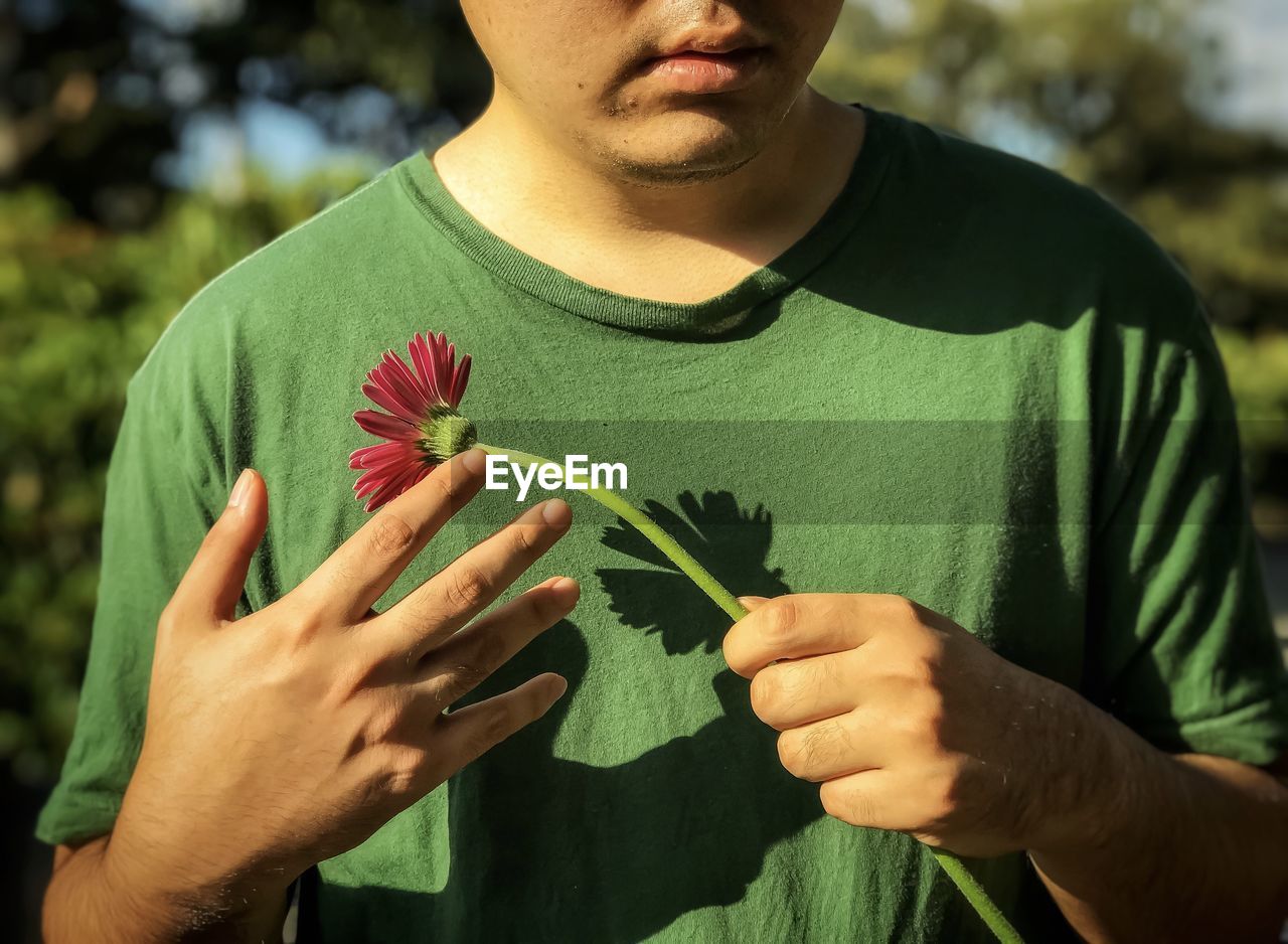 MIDSECTION OF MAN HOLDING LEAF AT HOME