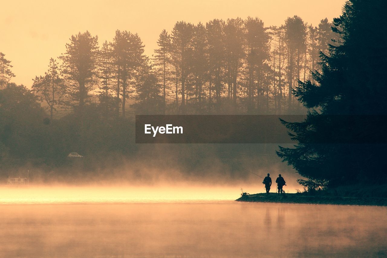 SILHOUETTE PEOPLE ON LAKE AGAINST SKY AT SUNSET