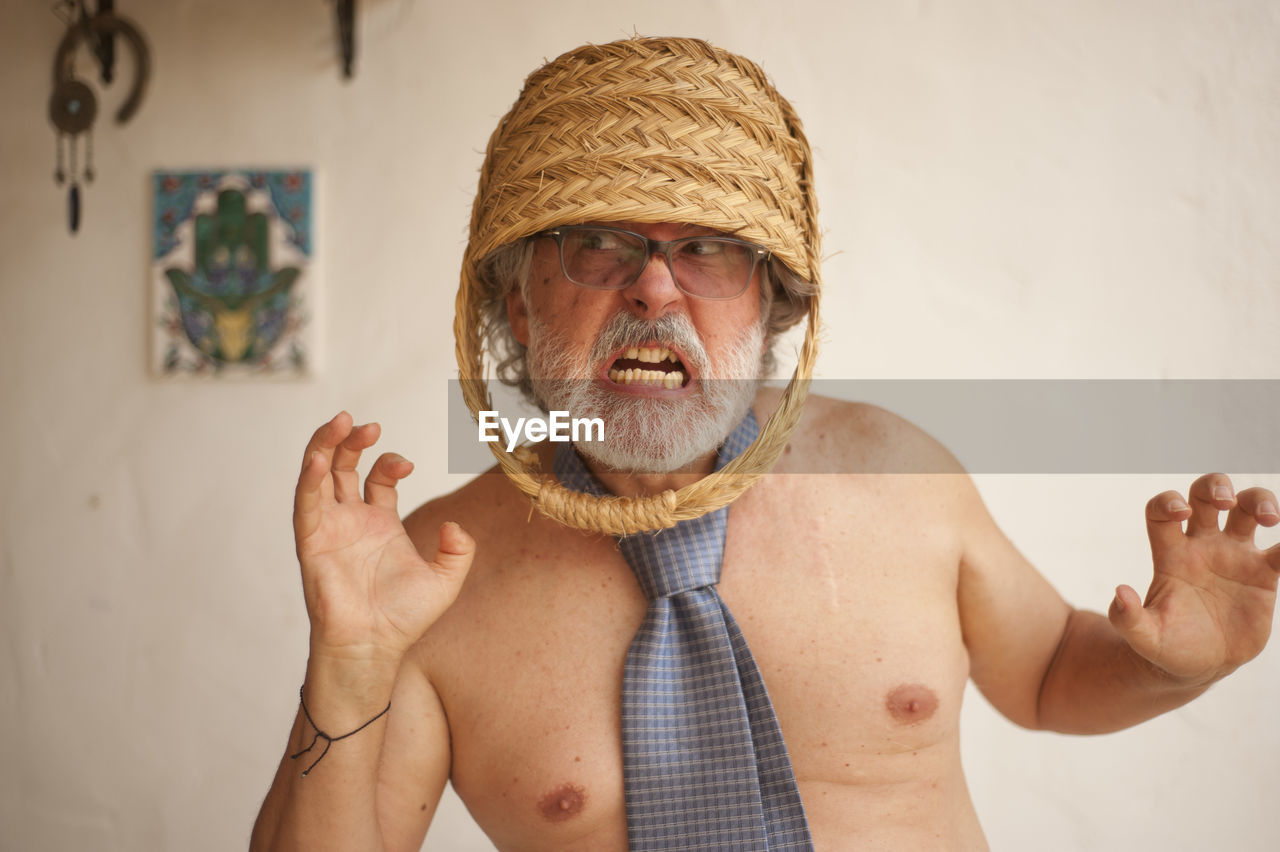 PORTRAIT OF SHIRTLESS MAN WEARING HAT STANDING AGAINST CURTAIN