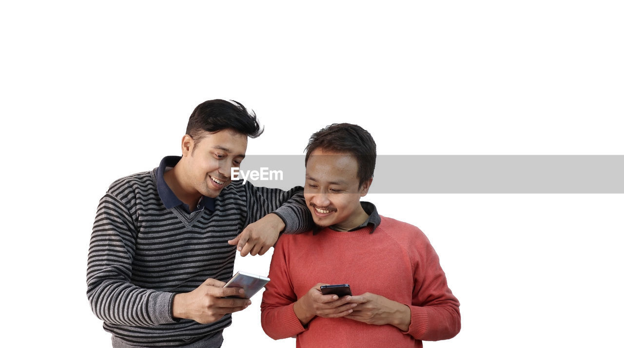 YOUNG MAN USING SMART PHONE AGAINST GRAY BACKGROUND