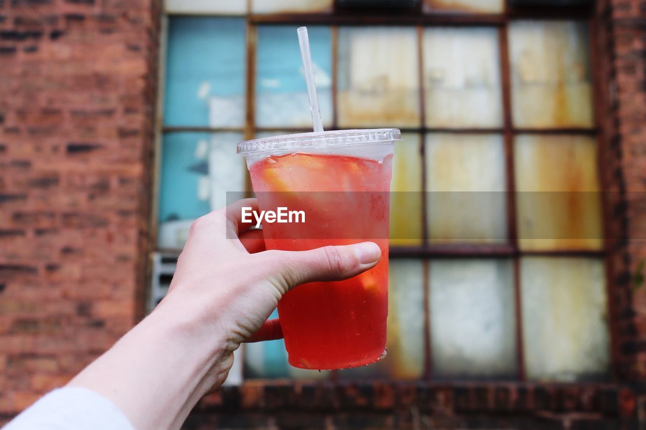 Cropped hand holding cocktail glass against window