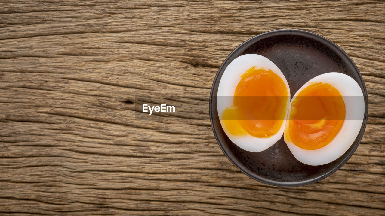 Superb runny yolk boiled egg in ceramic plate on rustic natural wood texture background, top view