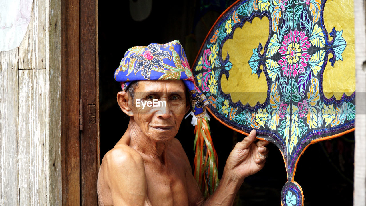 Portrait of shirtless man holding multi colored kite