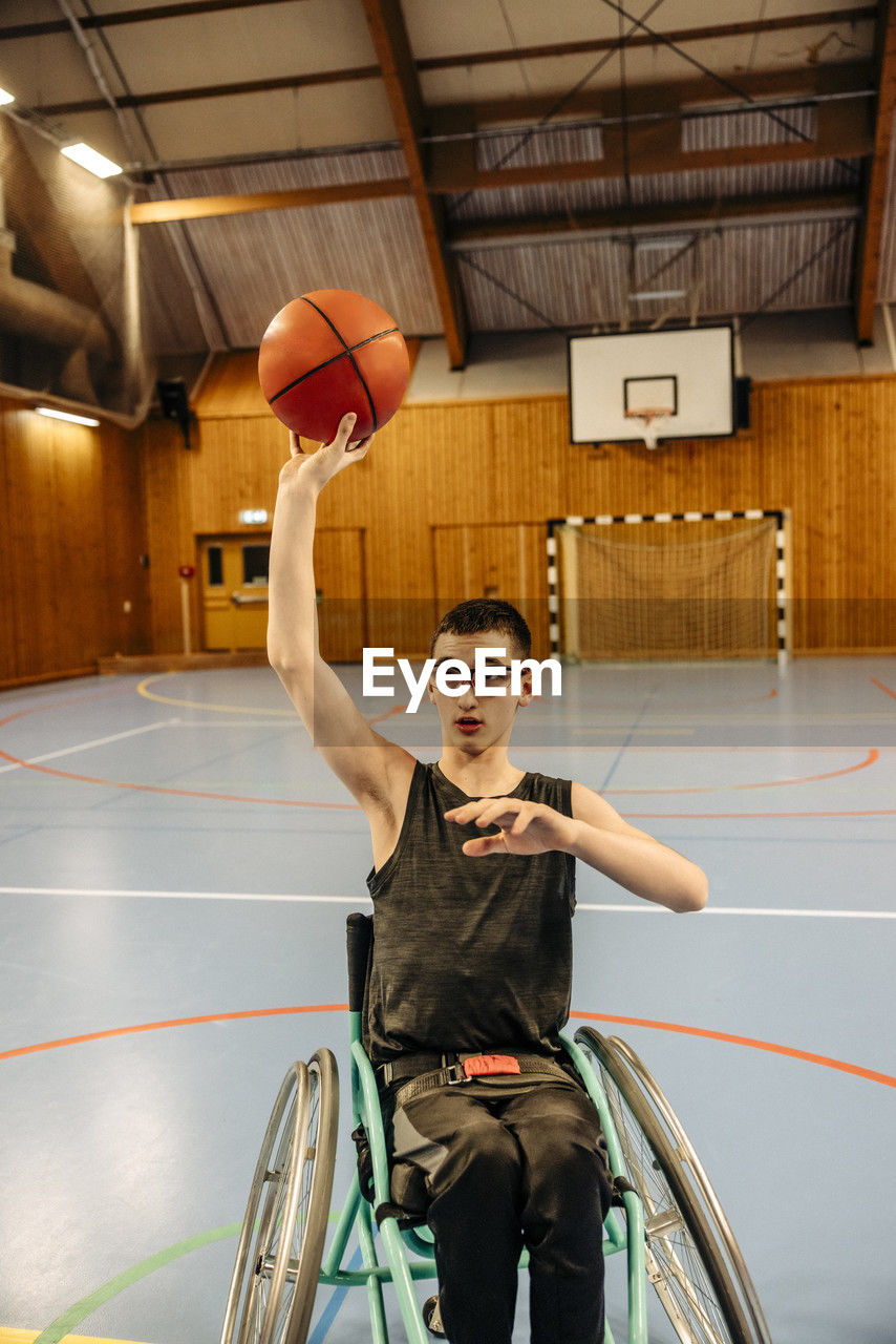 Girl with disability playing basketball while sitting on wheelchair at sports court
