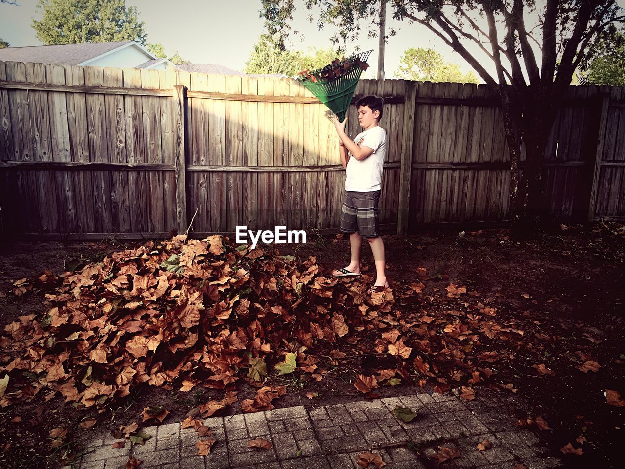 Boy with broom standing in yard against fence