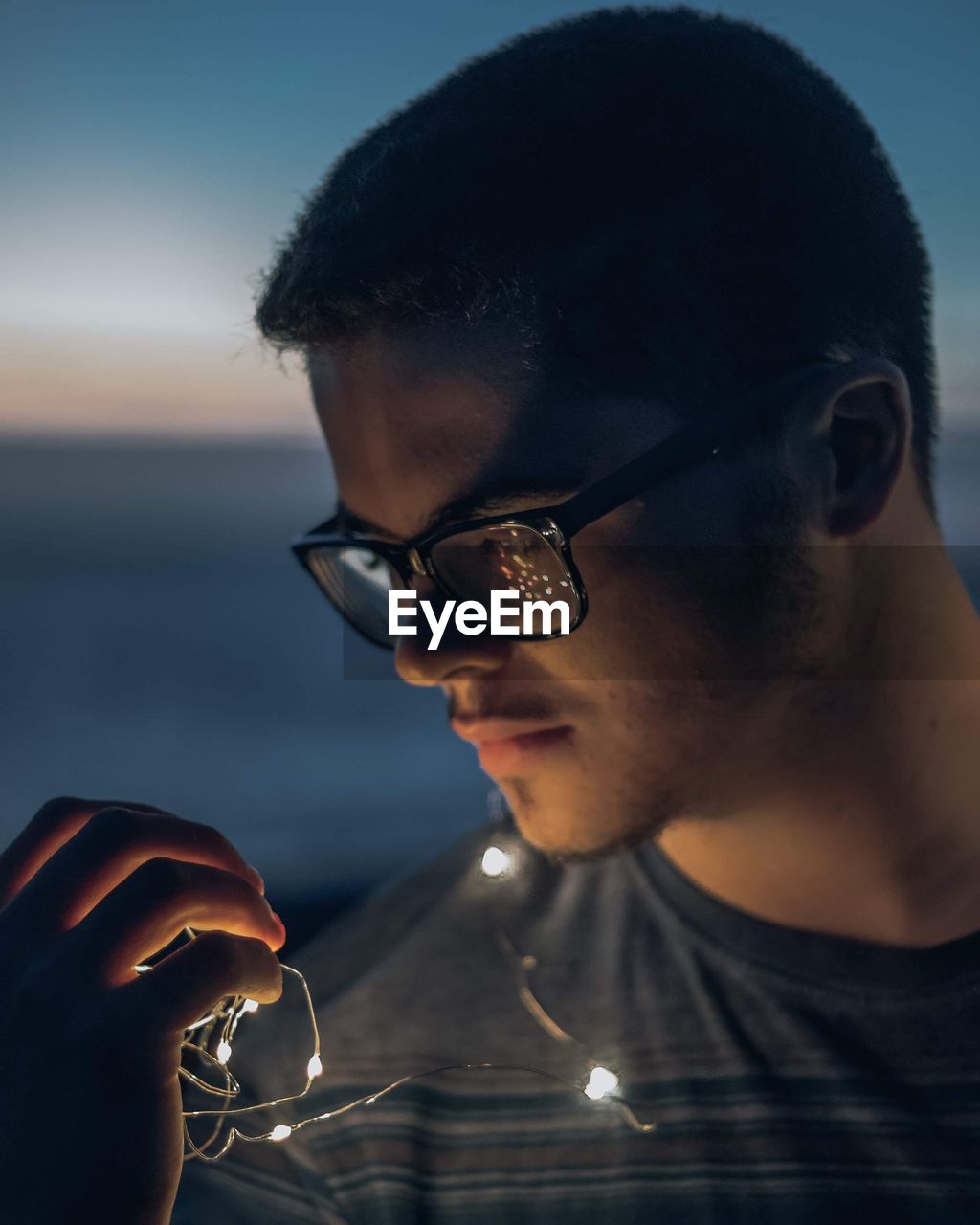 Close-up of young man holding illuminated string lights at night