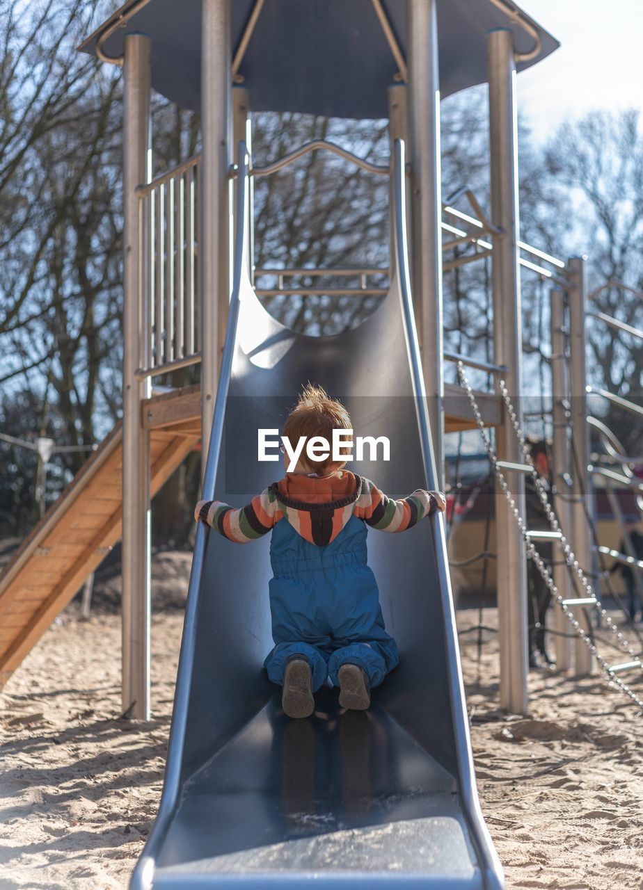 Rear view of boy sliding in park