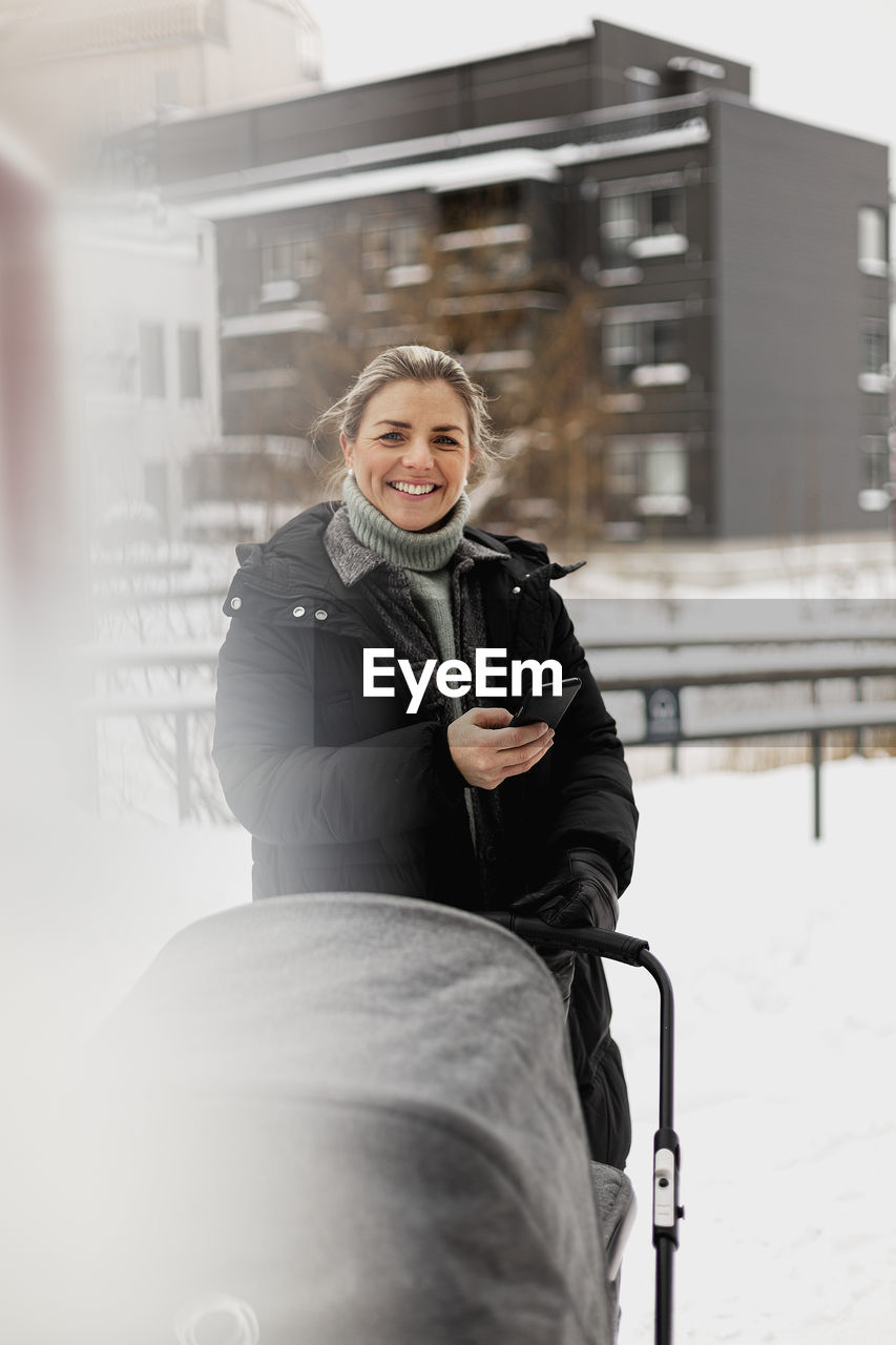 Smiling woman with pram holding cell phone