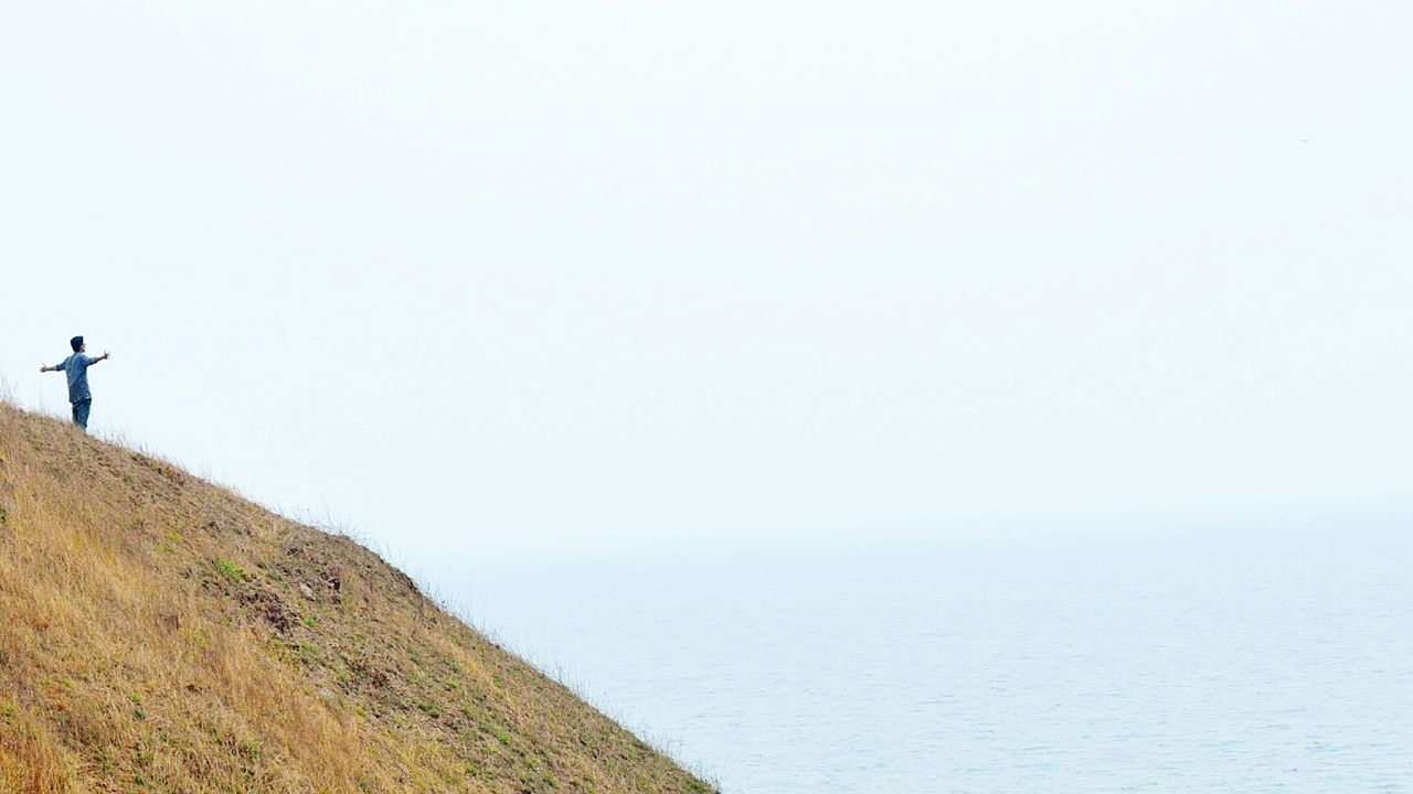 MAN LOOKING AT SEA SHORE AGAINST SKY