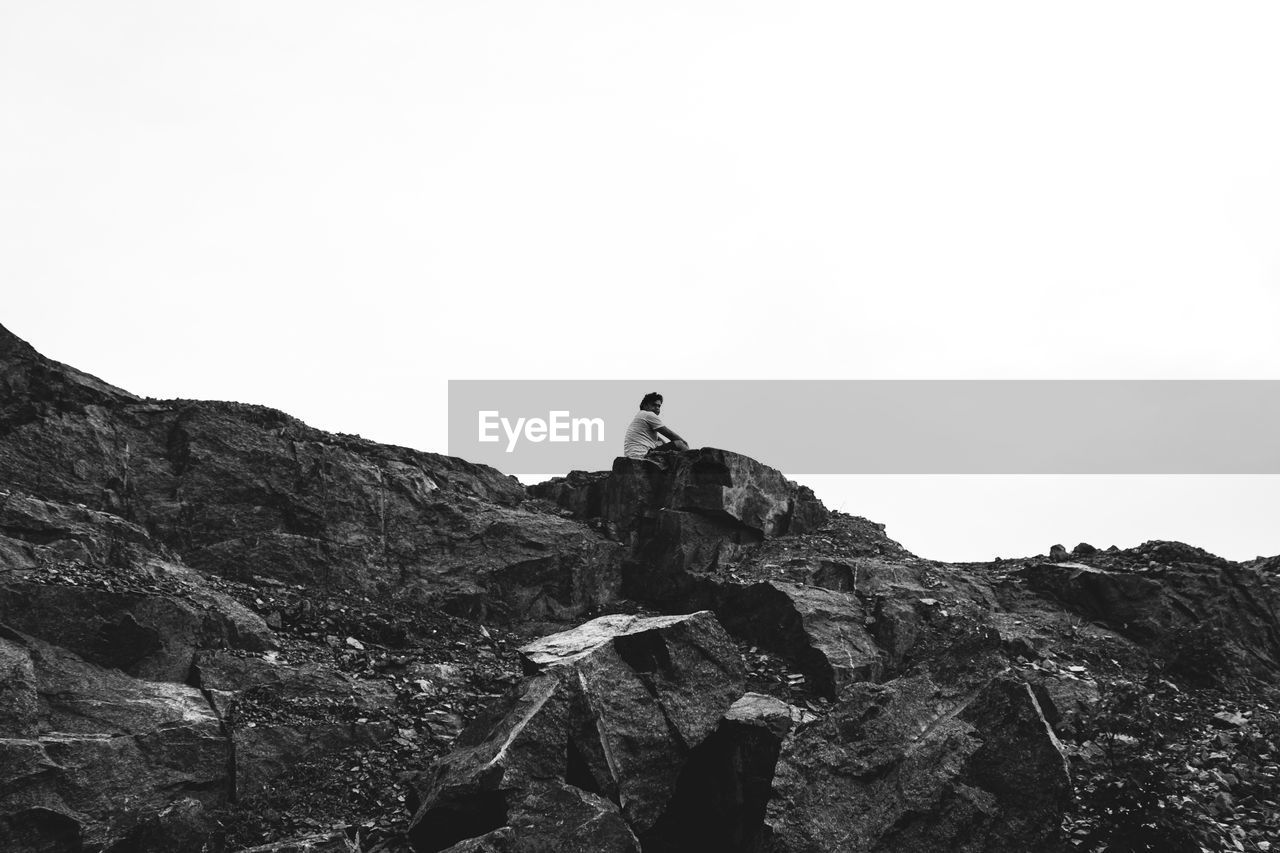 LOW ANGLE VIEW OF PERSON ON ROCKS AGAINST SKY