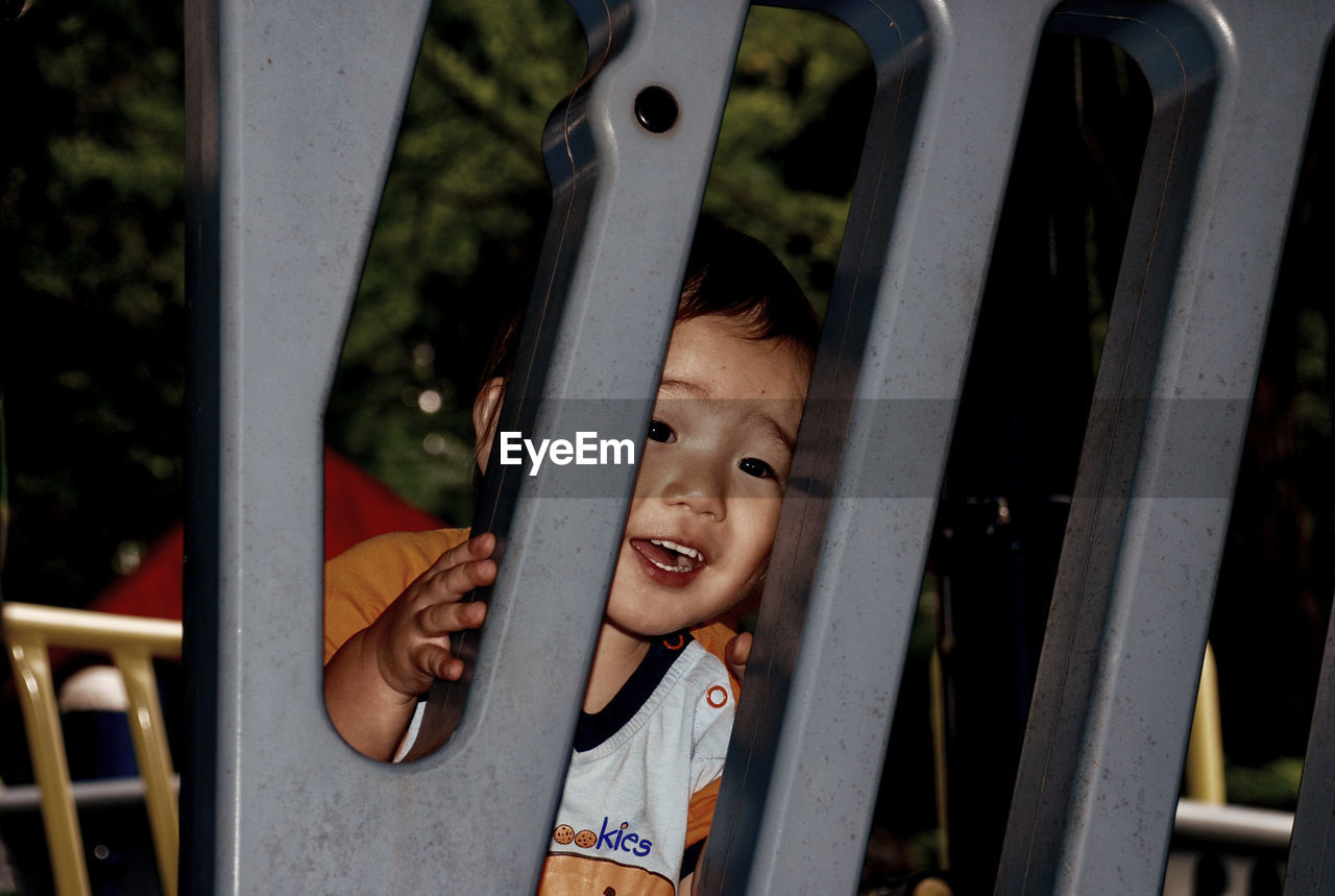 Cute boy looking through railing while playing at park