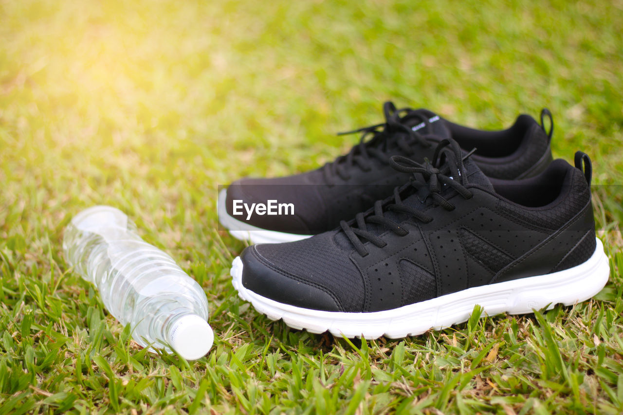 Close-up of shoes and water bottle on grass