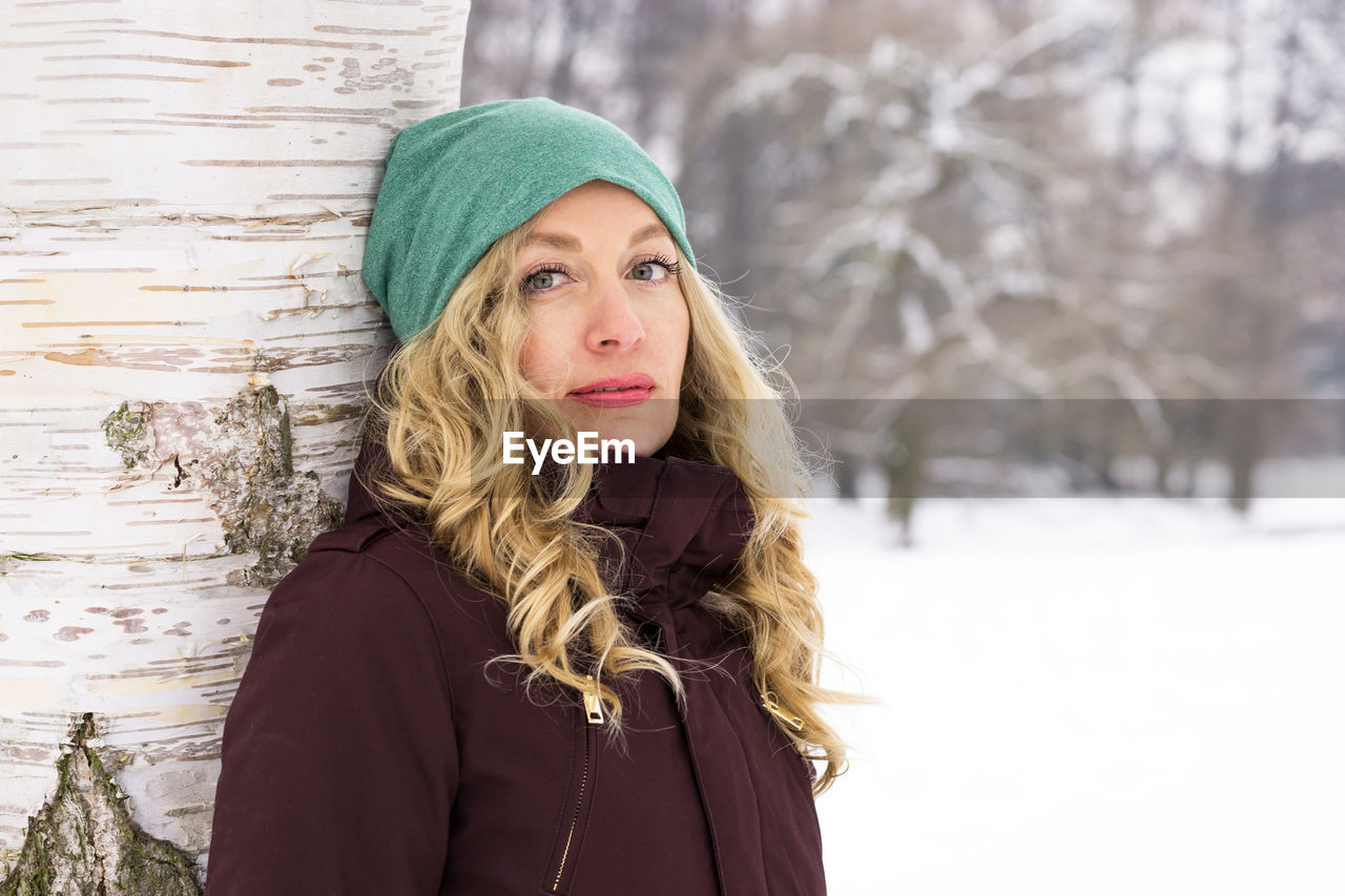 Portrait of smiling young woman standing by tree during winter