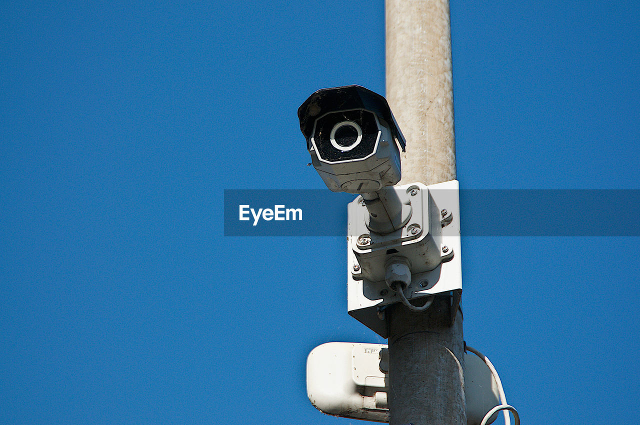 Low angle view of security camera at street against clear blue sky