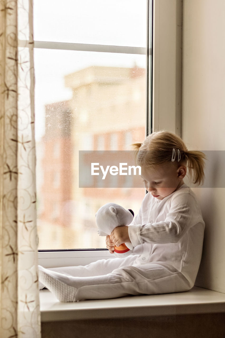 Full length of girl with stuffed toy sitting by window