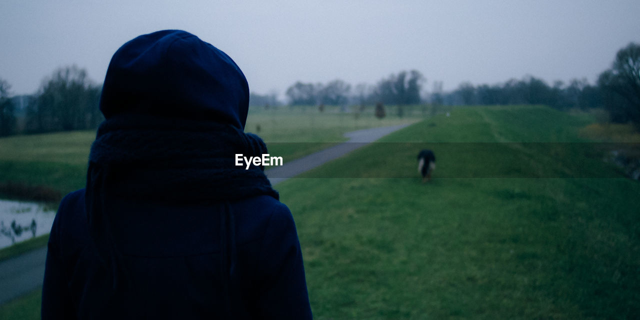 Rear view of woman standing by dog on grassy field