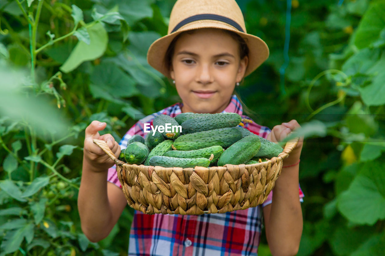 Girl holding cucumbers in basket against plants