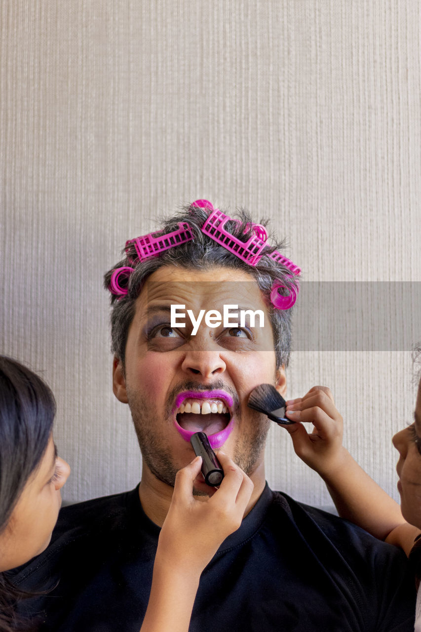 Cropped hands of children applying make-up on father face