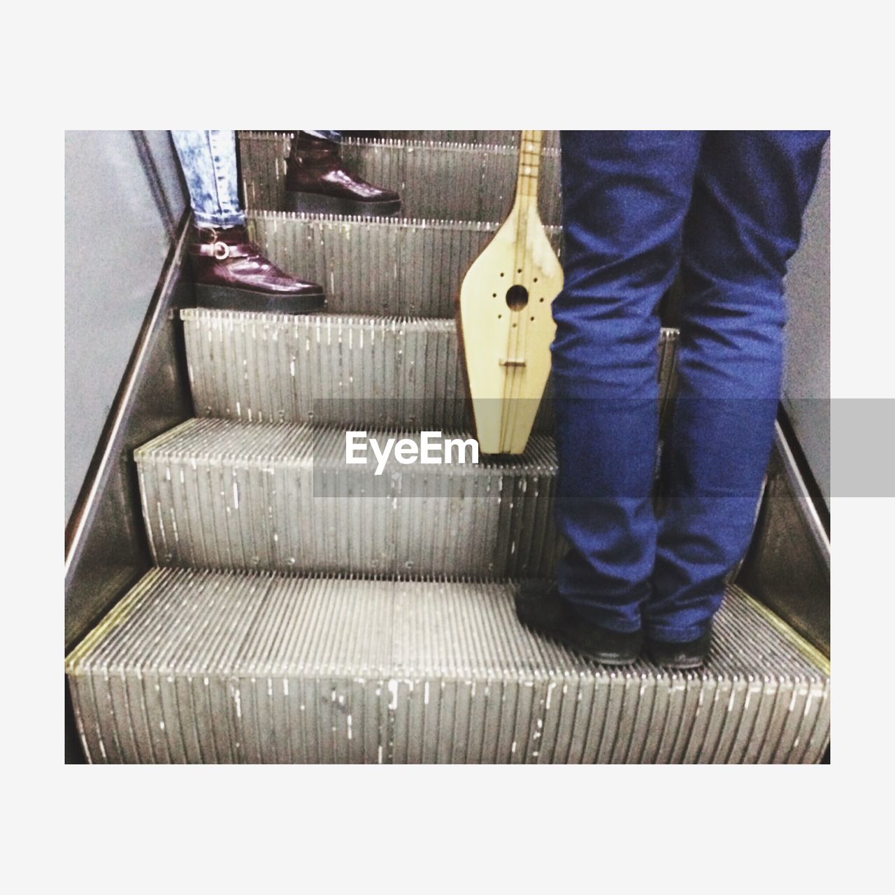 Low section of people with traditional string instrument on escalator