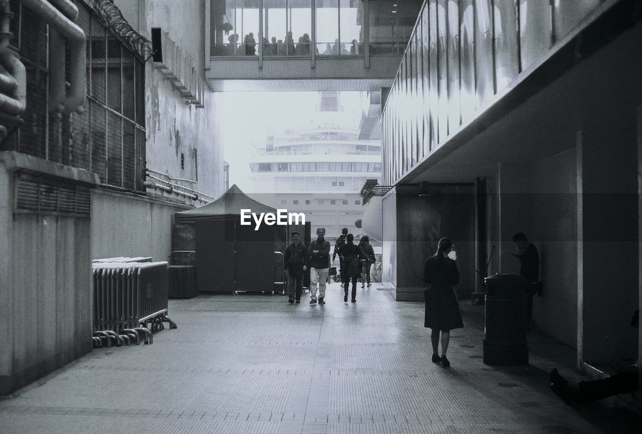 PEOPLE WALKING IN CORRIDOR ALONG BUILDINGS