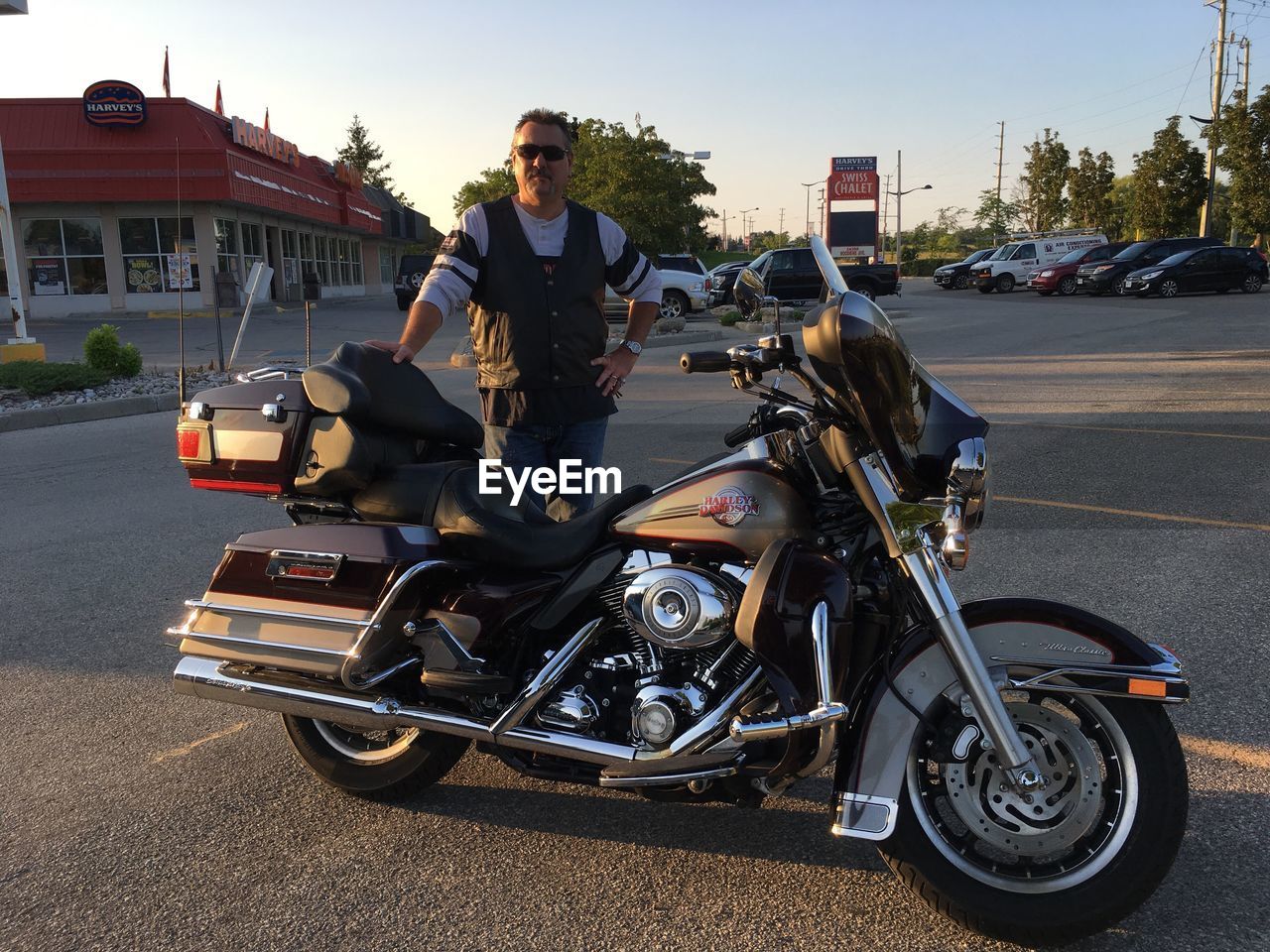 Portrait of man standing by motorcycle on road in city