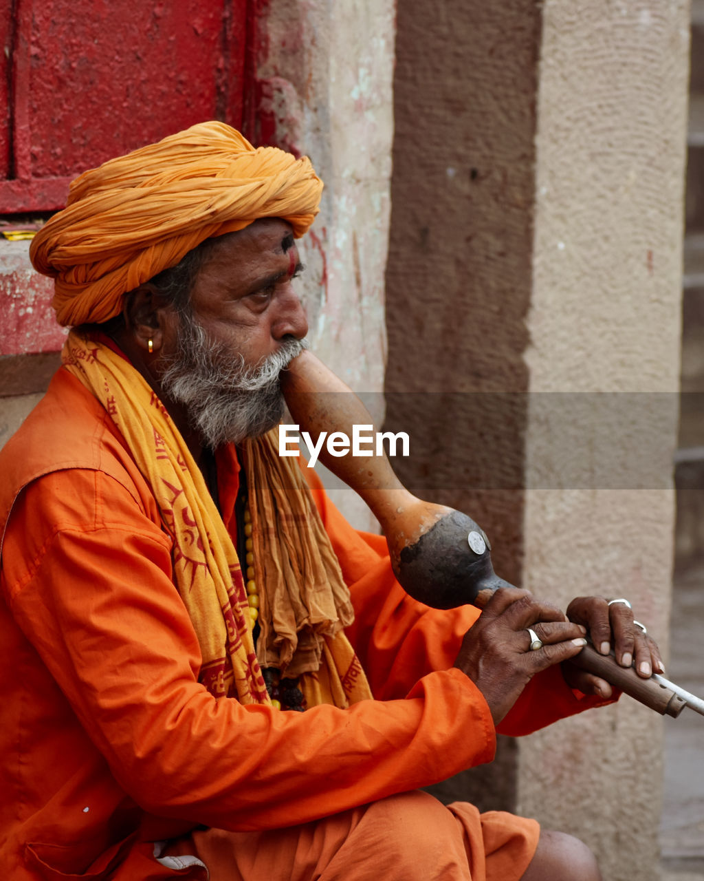 SIDE VIEW OF MAN LOOKING AT CAMERA WHILE SITTING ON ORANGE