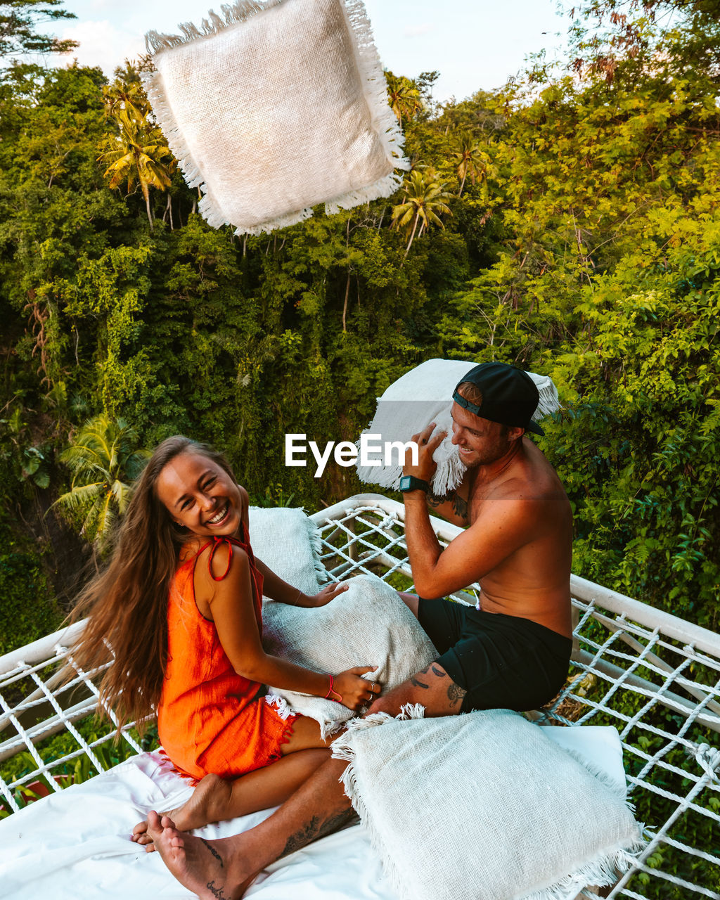 Couple having cute pillow fight on a netted bed above the jungle in bali