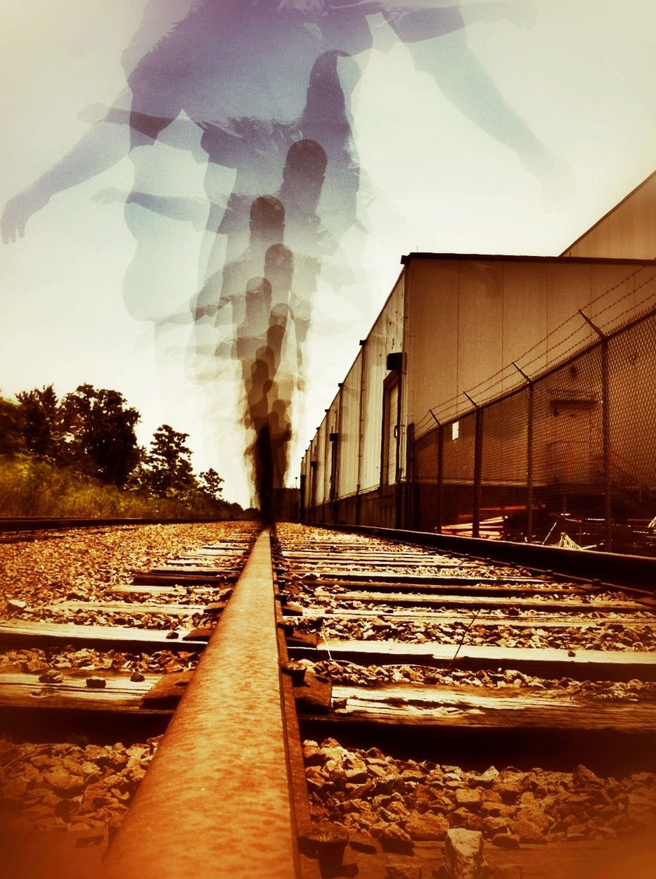 Multiple exposure of person balancing on railroad track against sky