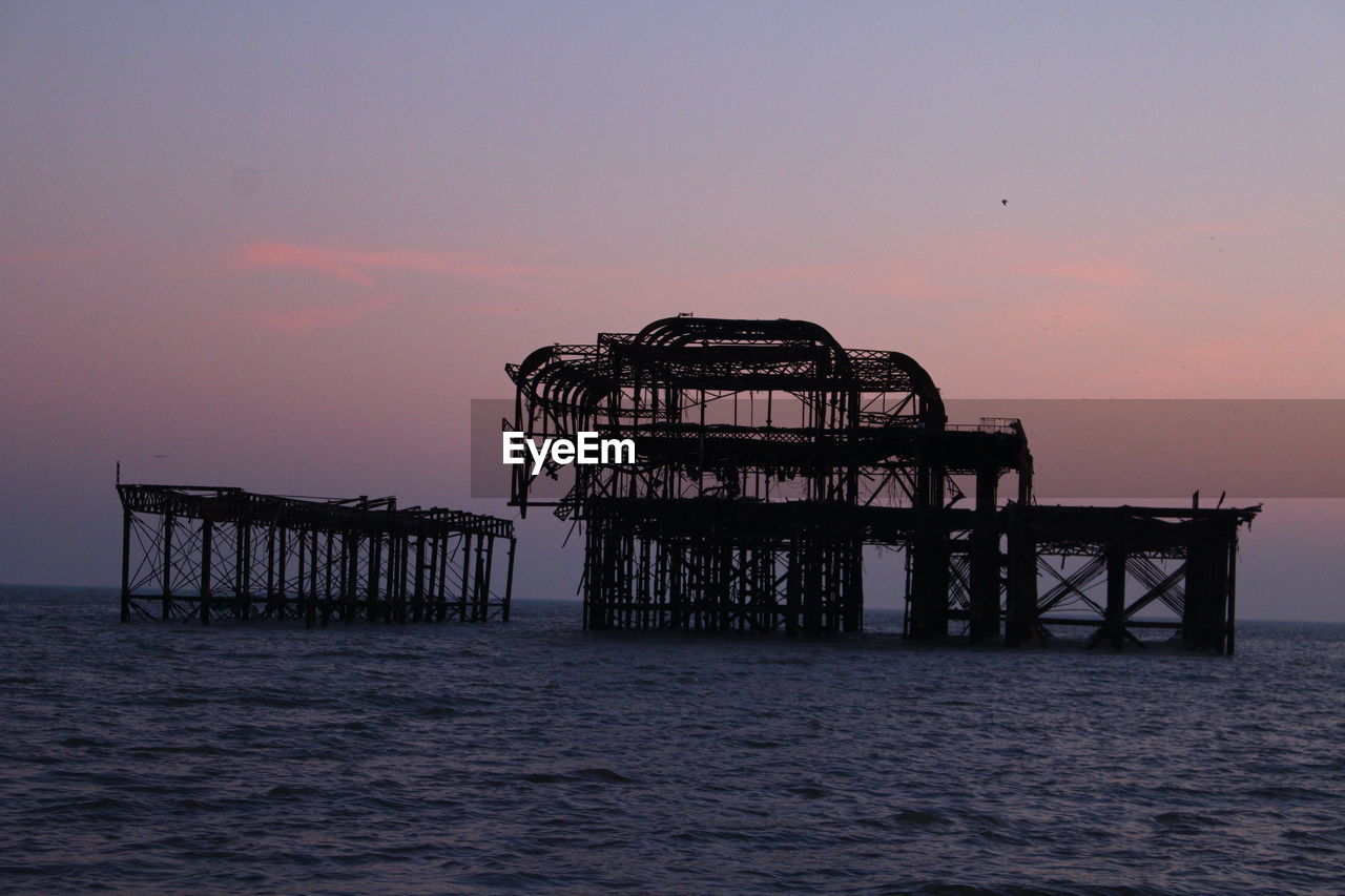 Broken metallic structure on sea against sky at dusk