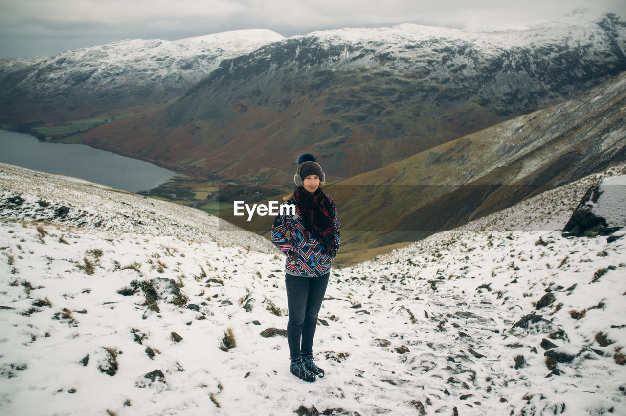 Young woman with hands in pockets standing on snow covered mountains