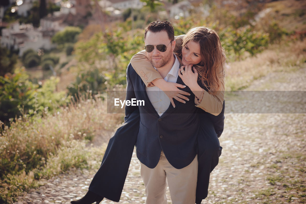 Man giving piggy back ride to happy woman standing on land