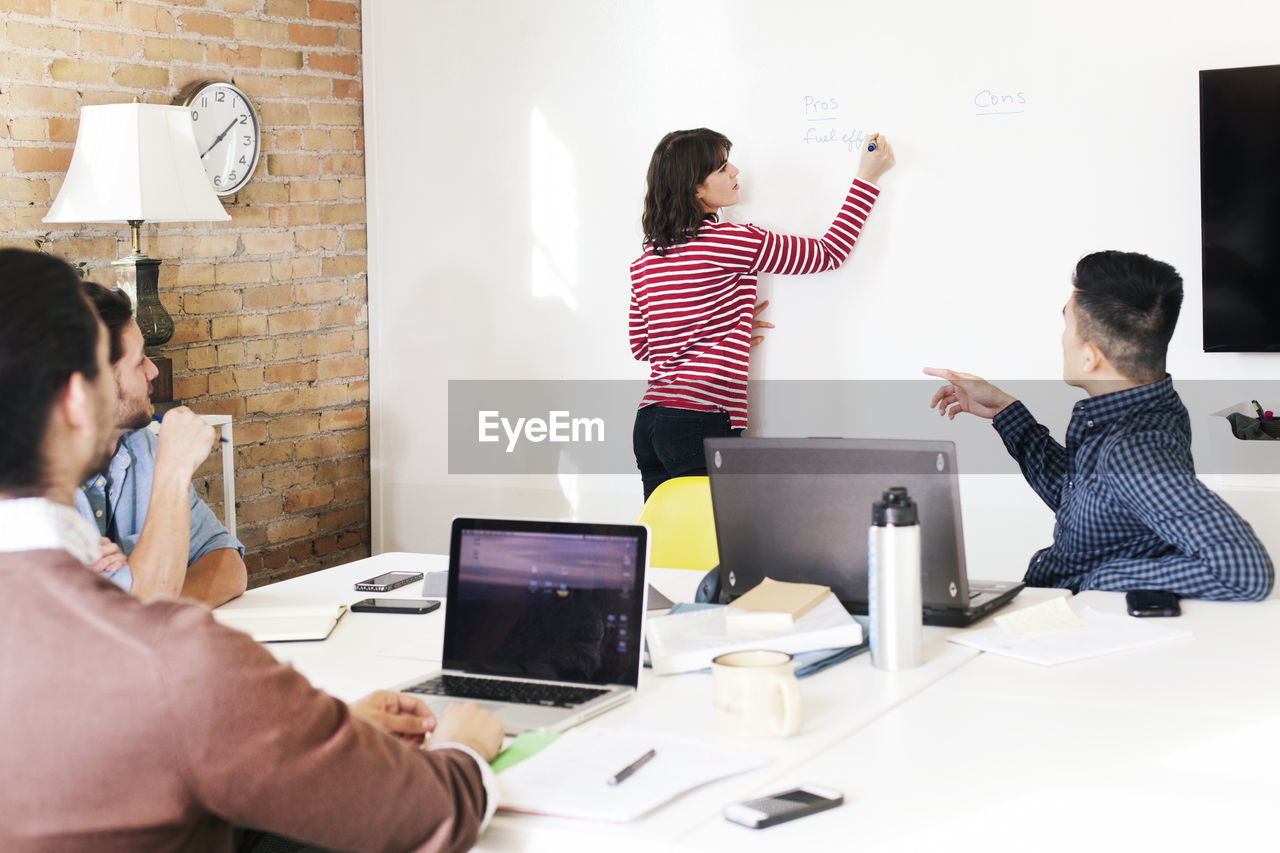 Colleagues looking at businesswoman writing on whiteboard during meeting in boardroom