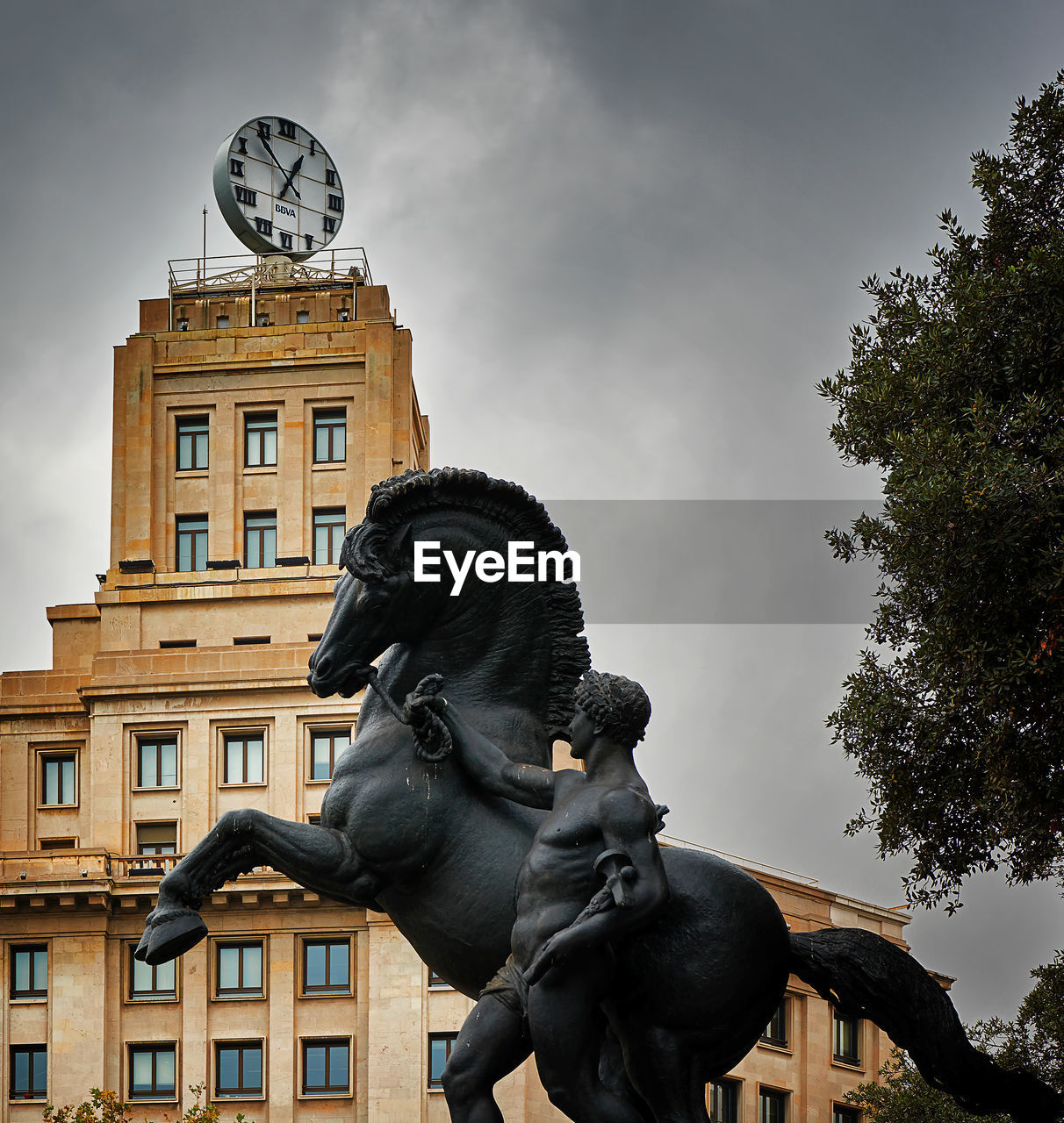Low angle view of horse and man statue against clock tower at placa de catalunya
