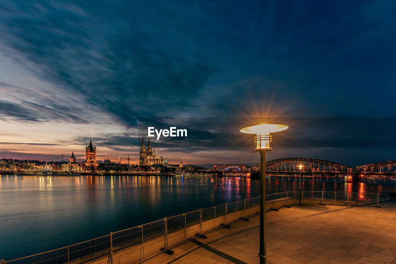 View of cologne cathedral with hohenzollern bridge at nightfall and a lamppost in the foreground, 