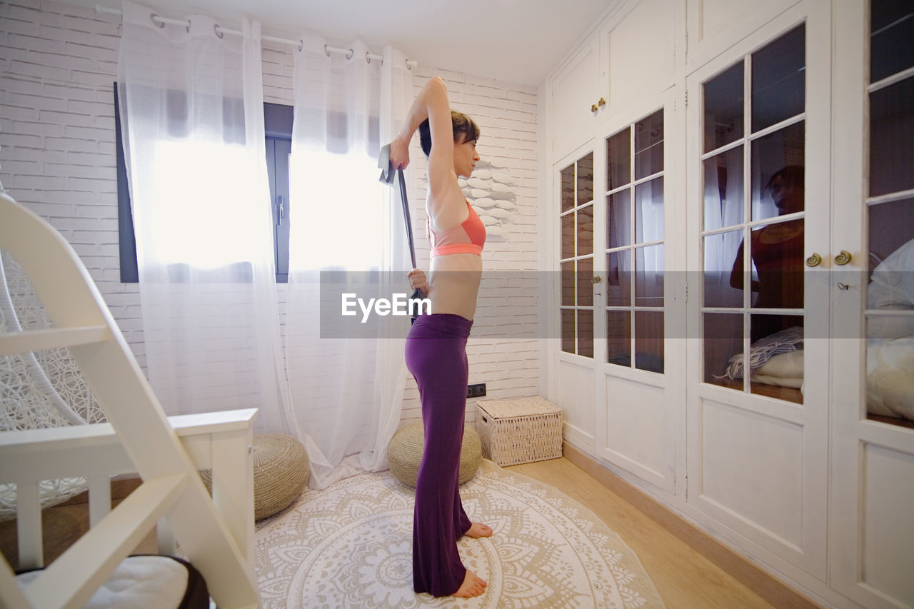 Side view of woman exercising while standing at home