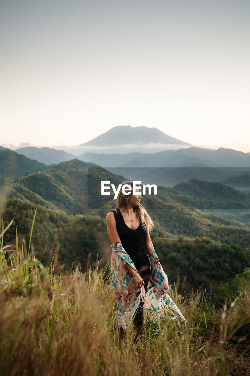 A blond woman is enjoying the beautiful view of mt. agung and the green surrounding.