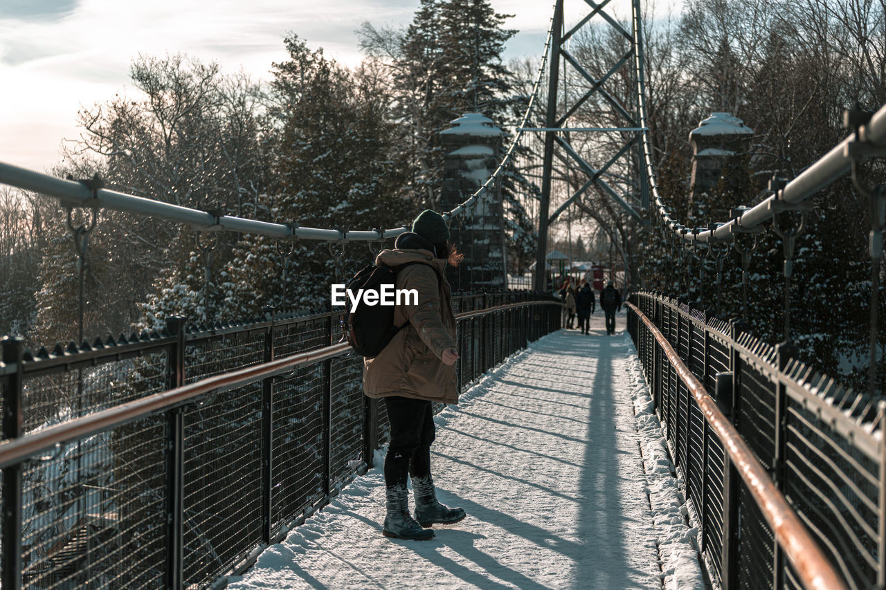 REAR VIEW OF MAN WALKING ON FOOTBRIDGE