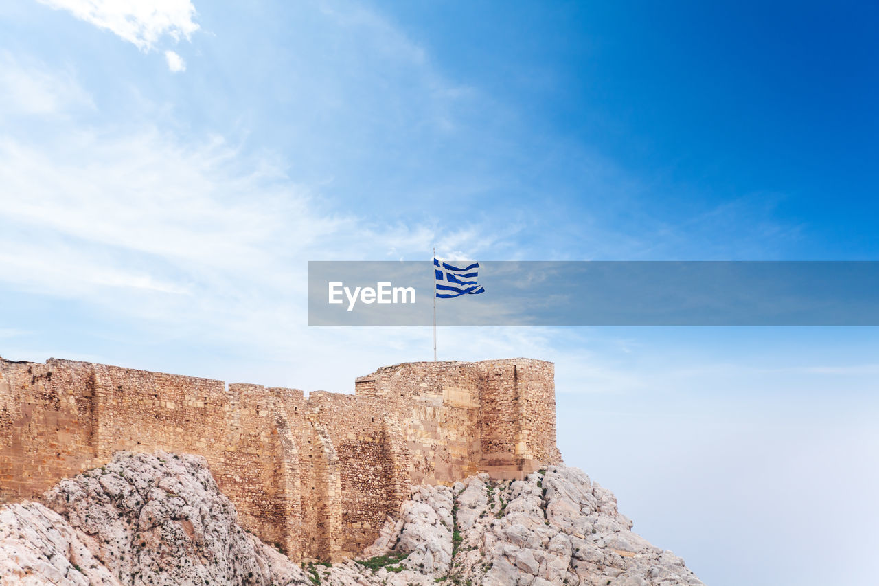 LOW ANGLE VIEW OF FLAG AGAINST ROCK FORMATION AGAINST SKY