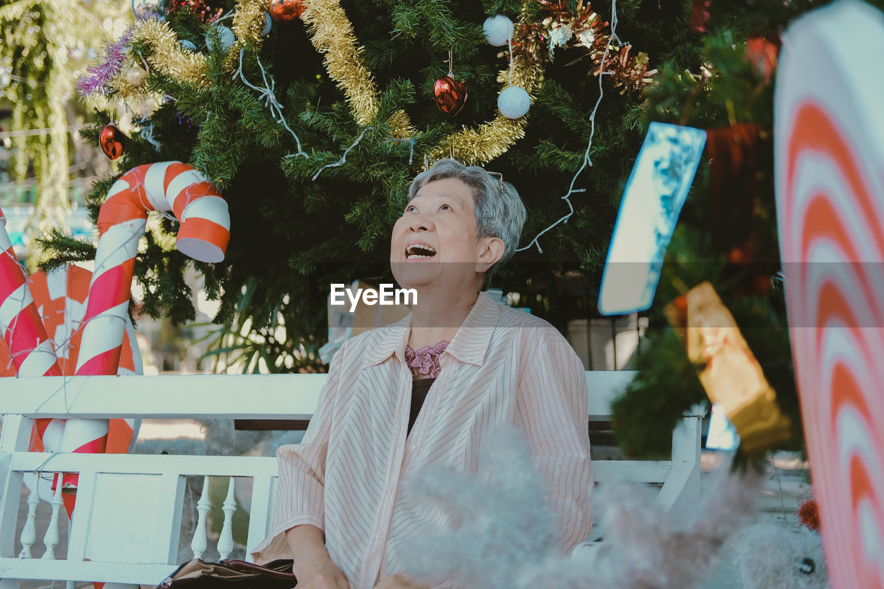 Cheerful senior woman sitting against christmas tree