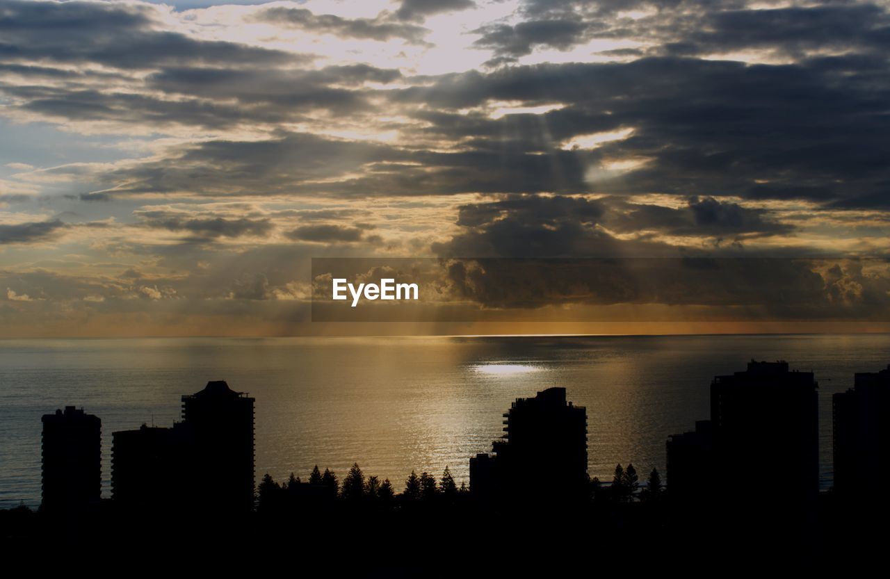 Silhouette buildings by sea against sky during sunset