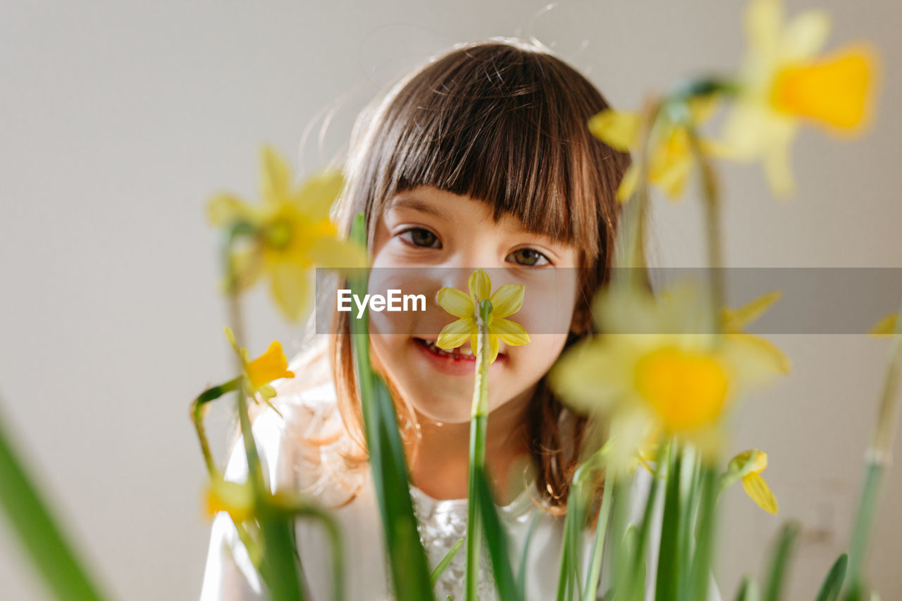Smiling little girl behind bright yellow daffodil flowers