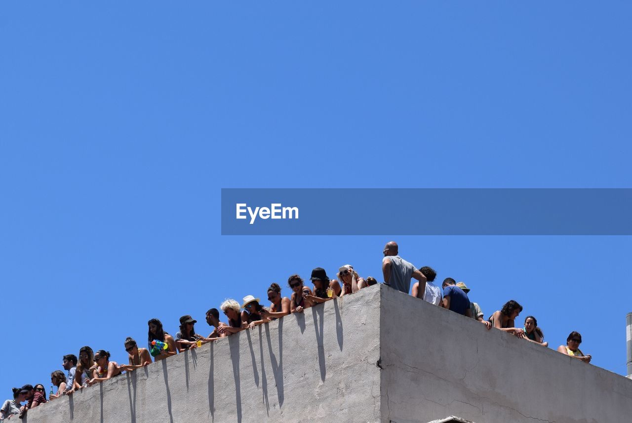 Low angle view of people standing by railing of building against clear sky