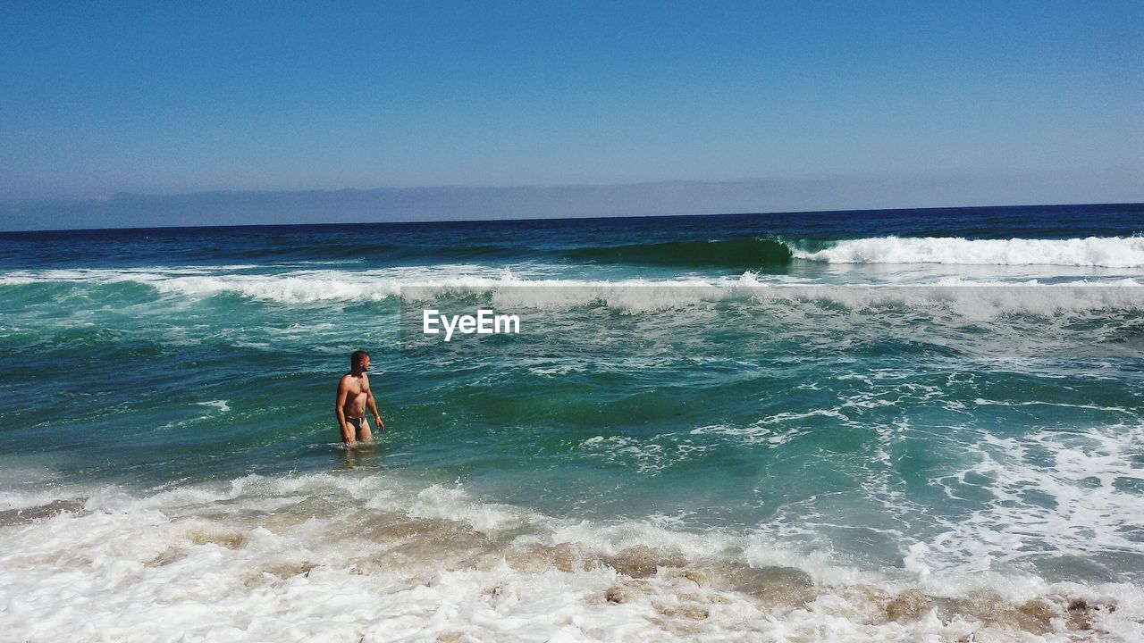 Shirtless man standing in sea against sky