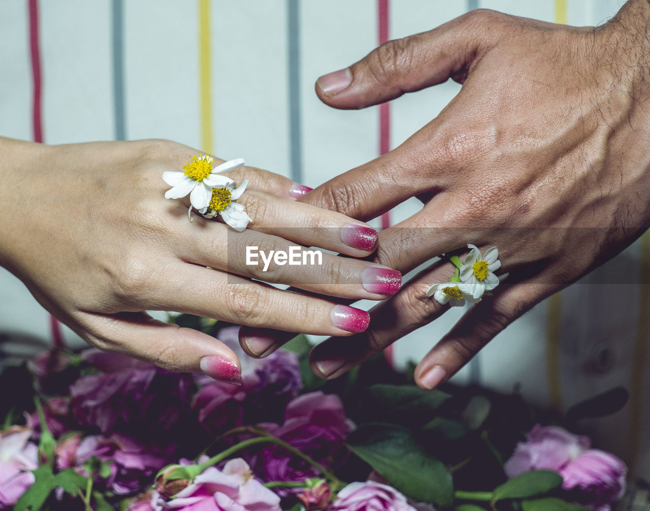 Cropped hands of bride and bridegroom holding white flowers during wedding