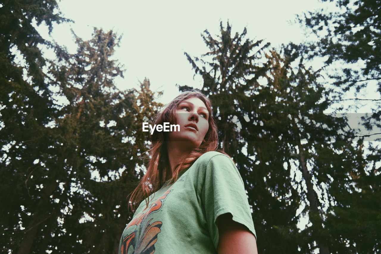 Low angle view of young woman standing against trees