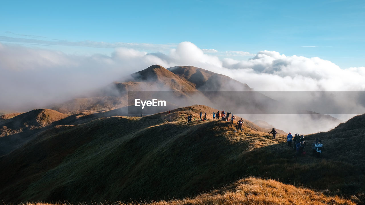 People hiking on mountain against cloudy sky