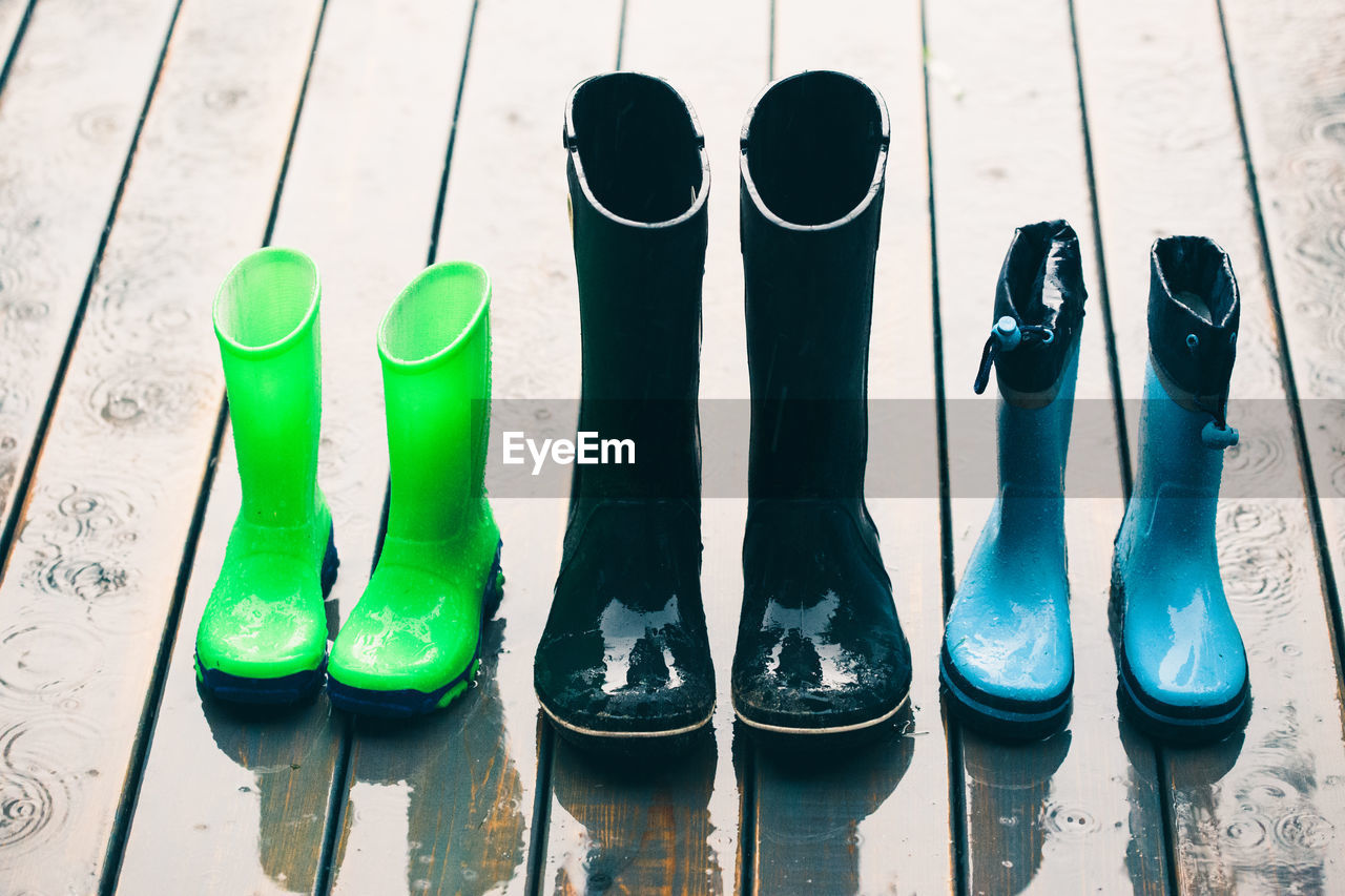 Row of wellies in various sizes standing on a wooden porch while raining